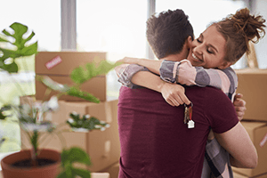 couple hugging holding keys surrounded by moving boxes