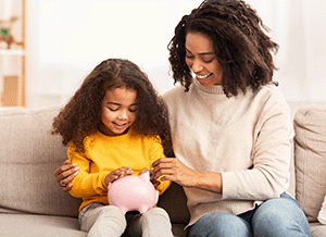 Mother teaching young daughter to save with piggy bank.